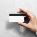 Hand holding blank white credit card mockup with black magnetic stripe, back side view. Plastic bank-card design mock up with magstripe.